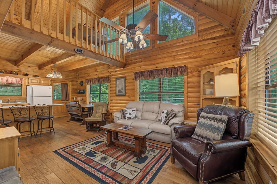 Relax in this warm, sunlit cabin with soaring wood ceilings, a cozy leather armchair, and views of leafy greenery. Your perfect rustic retreat awaits.