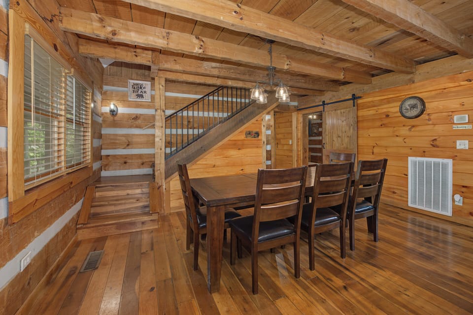 Gather around the solid wood dining table under rustic timber beams, perfect for family meals and game nights in this warm, open-plan cabin retreat.