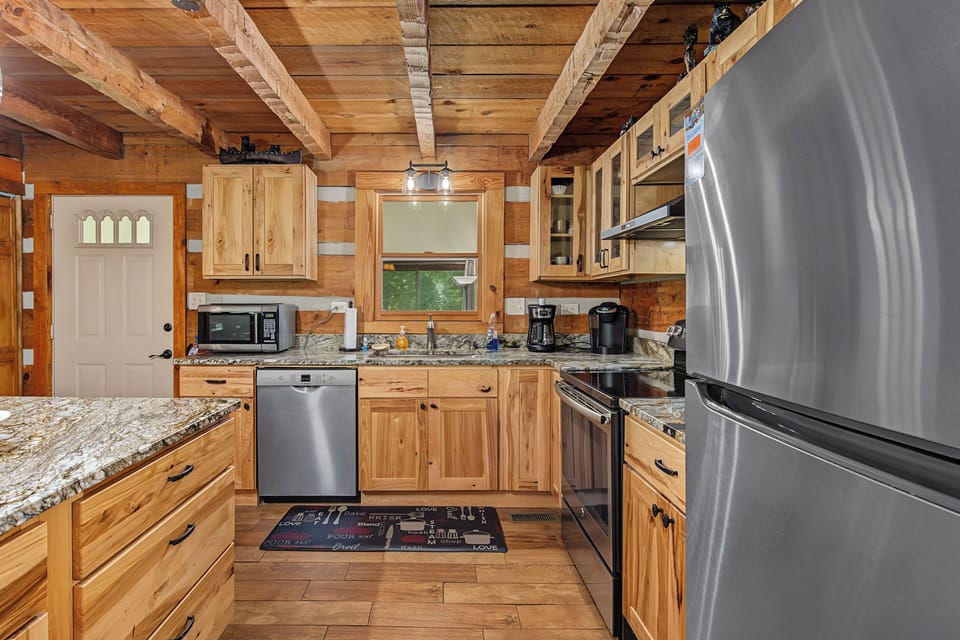 Your fully equipped kitchen features granite countertops, stainless steel appliances, and rustic wood cabinetry beneath exposed beam ceilings—perfect for preparing meals together during your mountain getaway.