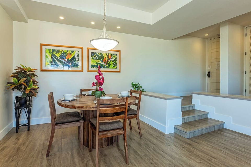 Gather around the warm wooden table beneath soft lighting, where tropical artwork and fresh blooms set the scene for memorable meals together.