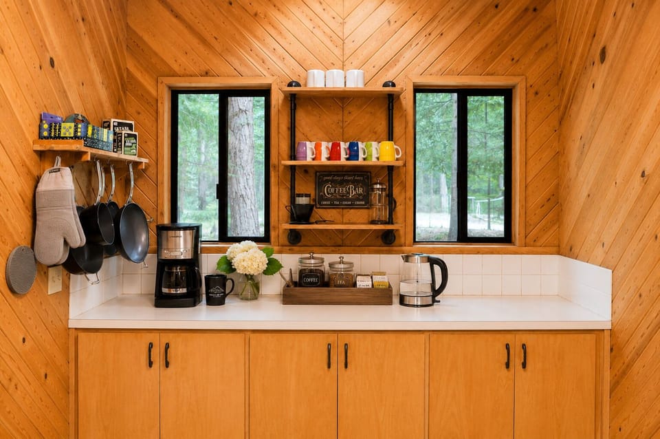 Your own coffee bar awaits, complete with colorful mugs, a French press, and forest views through the windows—perfect for savoring mornings in this cozy cabin retreat.