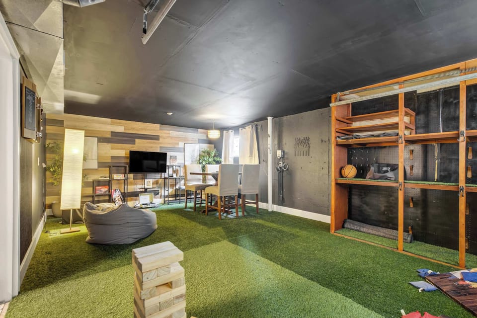 A wood accent wall and open shelving frame this wider view of the game room, a round pouf and wood crate stools adding extra casual seating across the turf, plenty of space for the whole group to spread out.
