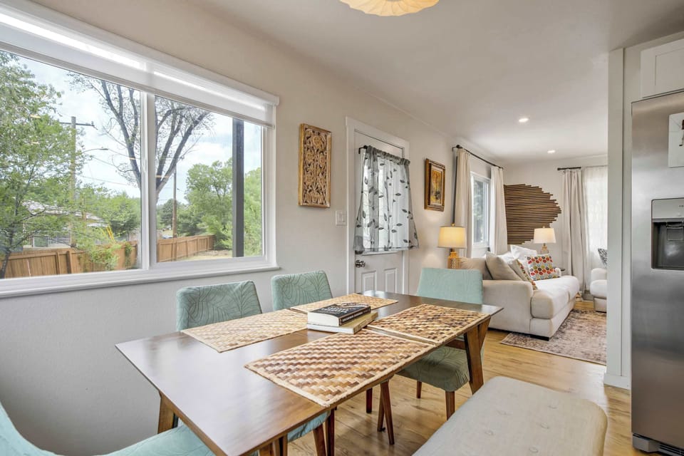 Corner windows wrap this dining nook in light, framing tree lined views behind a wood table set for eight. Woven chairs and a pair of textured wall hangings add warmth without crowding the crisp white walls.
