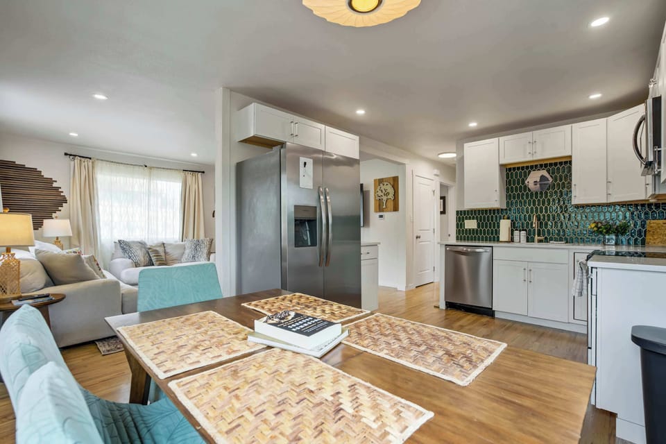 White shaker cabinets wrap the kitchen corner, the green hexagonal backsplash adding a playful pop of color, while the dining table just beyond keeps the whole open layout feeling like one connected gathering space.
