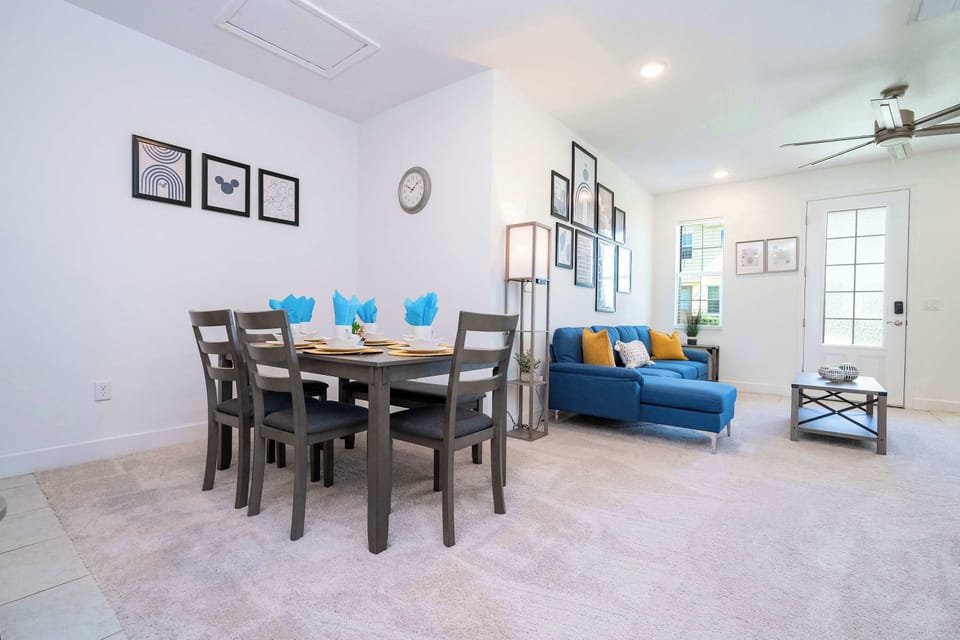 Spacious dining area with a modern table, blue napkins, and a cozy living room setup, perfect for family gatherings or casual meals.