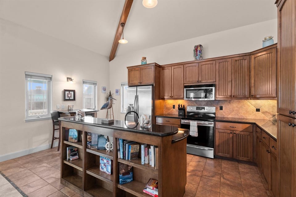 Fully equipped kitchen with granite island, stainless steel appliances, wood cabinetry, microwave, oven, and open shelving.