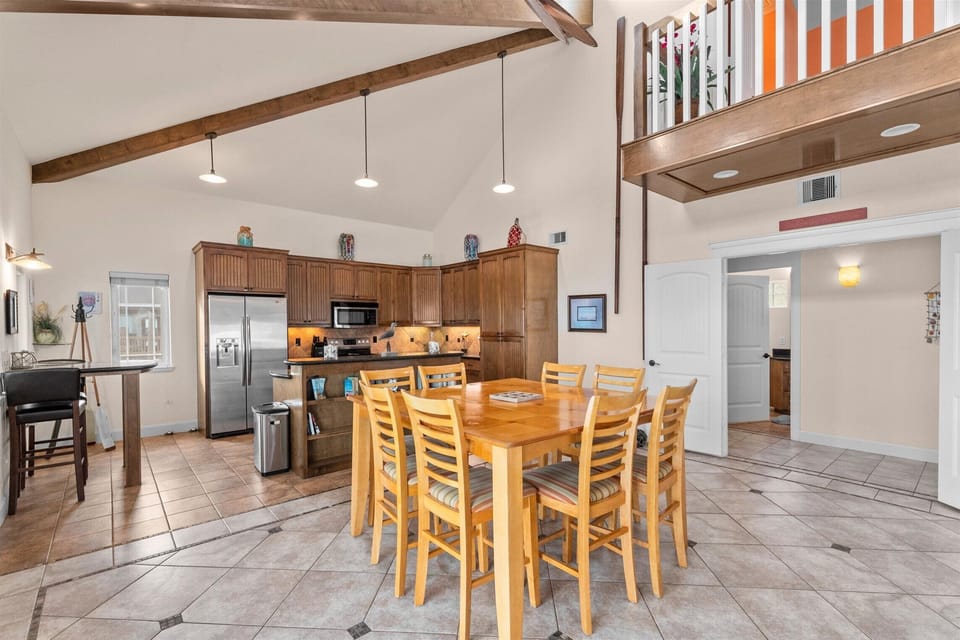Open dining and kitchen area with large wood table, bar-height seating, vaulted ceiling, stainless appliances, and spacious layout.