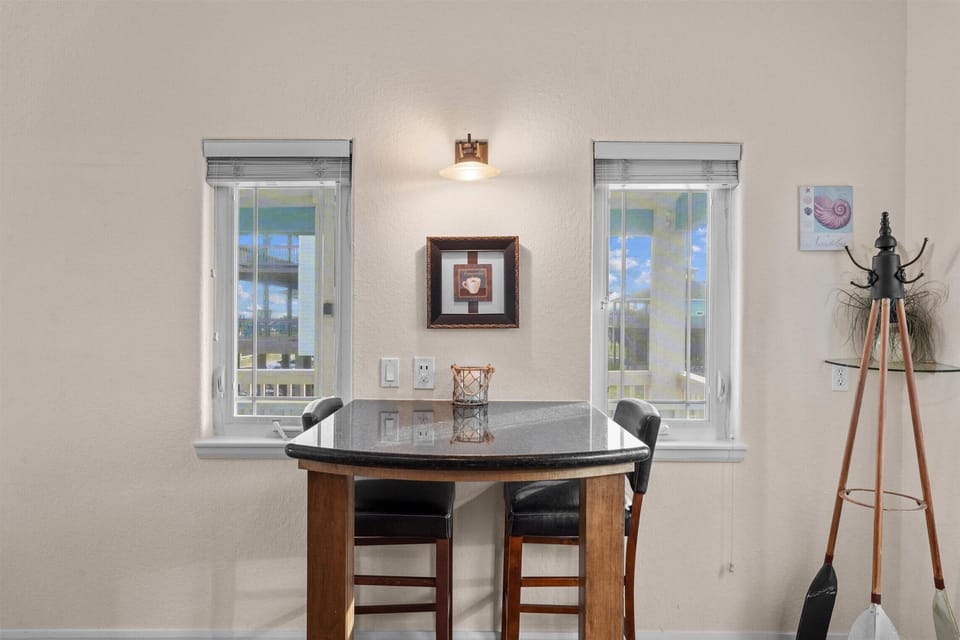 Intimate breakfast bar with granite tabletop, two stools, wall lighting, and windows bringing natural light into the dining area.