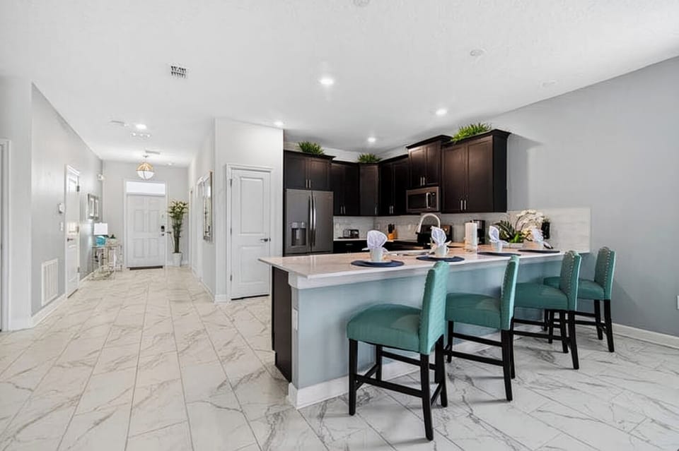 Modern kitchen with dark cabinetry, an island, and stylish teal barstools.