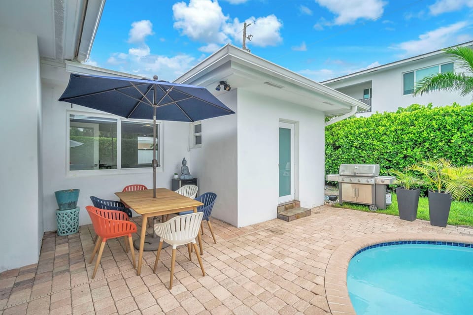 Poolside dining nook with umbrella shade, BBQ grill, and lush privacy hedges.