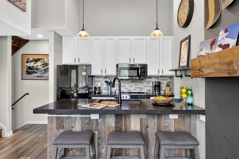 Sleek chef’s kitchen showcasing contrasting white cabinets, dark countertops, and a rustic reclaimed-wood breakfast bar.