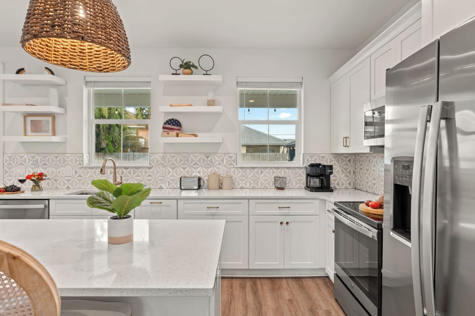 Bright coastal kitchen with island seating, woven pendants, and full appliances for easy group meals.