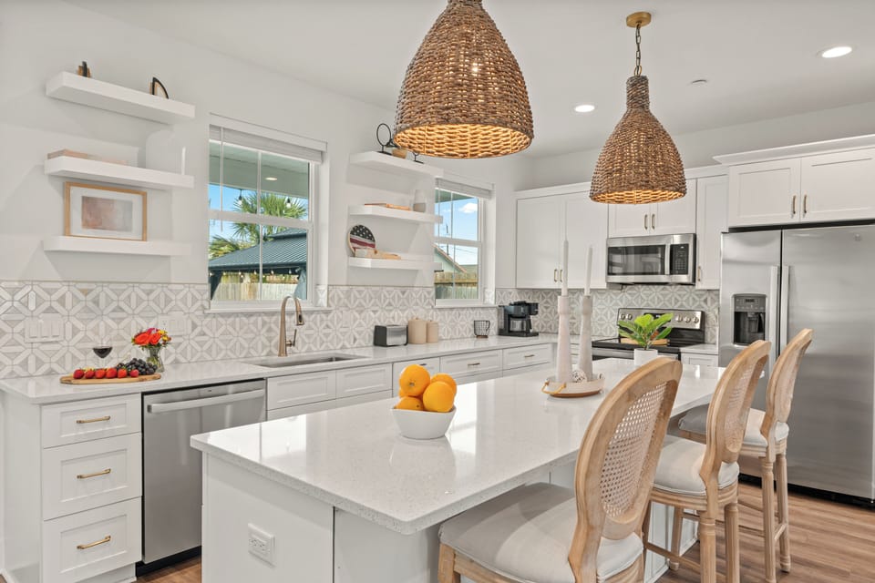 Bright coastal kitchen with island seating, woven pendants, and full appliances for easy group meals.