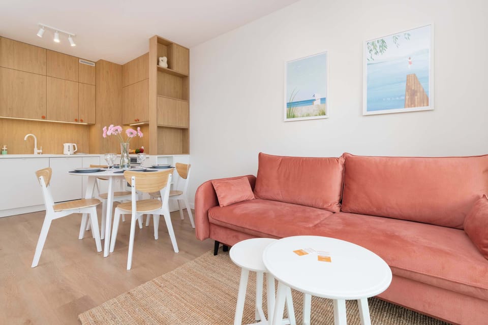 A wide-angle view displays the open-concept layout connecting the pink sofa to the kitchen space. Two coastal-themed art prints hang on the wall.