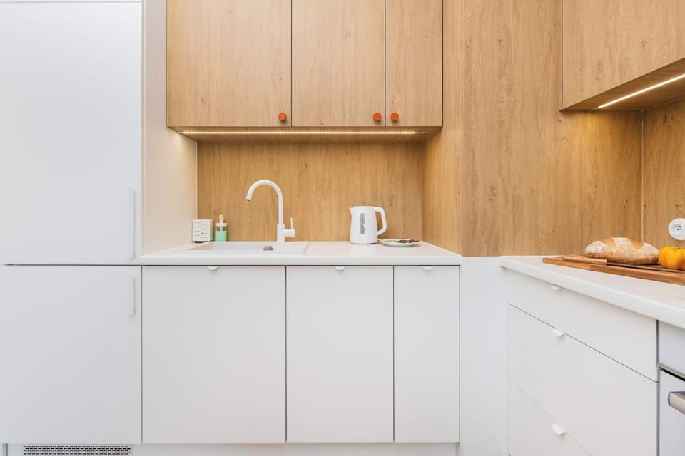 A sleek white kitchen counter features a chrome faucet and a white electric kettle. Built-in upper cabinets provide a clean, integrated look.