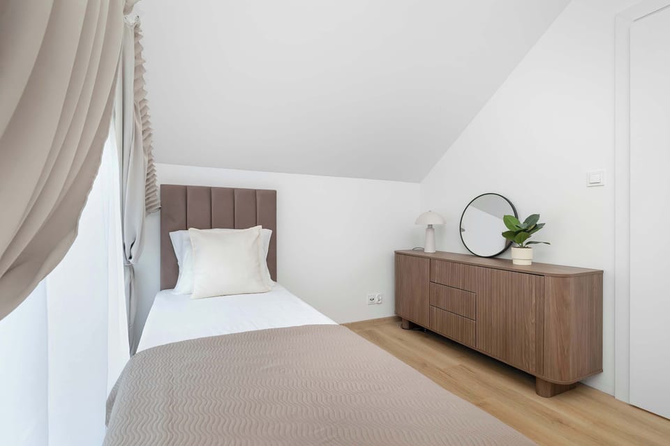 A cozy bedroom with a single beds, wooden flooring, and a simple modern dresser.