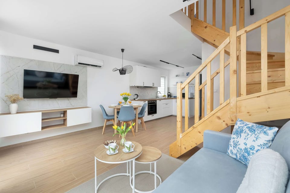 An airy interior shot looking from the living area towards the modern kitchen and the staircase. Clean white walls and minimalist furniture emphasize the spacious layout.