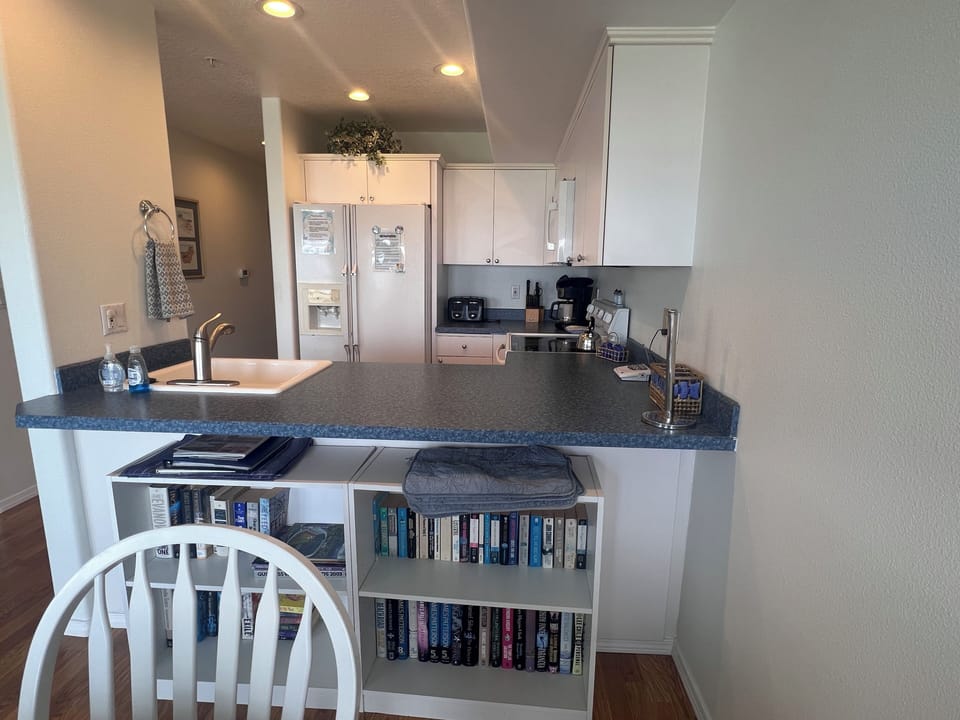 Your open-concept retreat awaits, where the kitchen flows seamlessly into bright living spaces. Enjoy thoughtful touches like a curated bookshelf, modern appliances, and ample counter space—perfect for morning coffee or preparing a meal together.