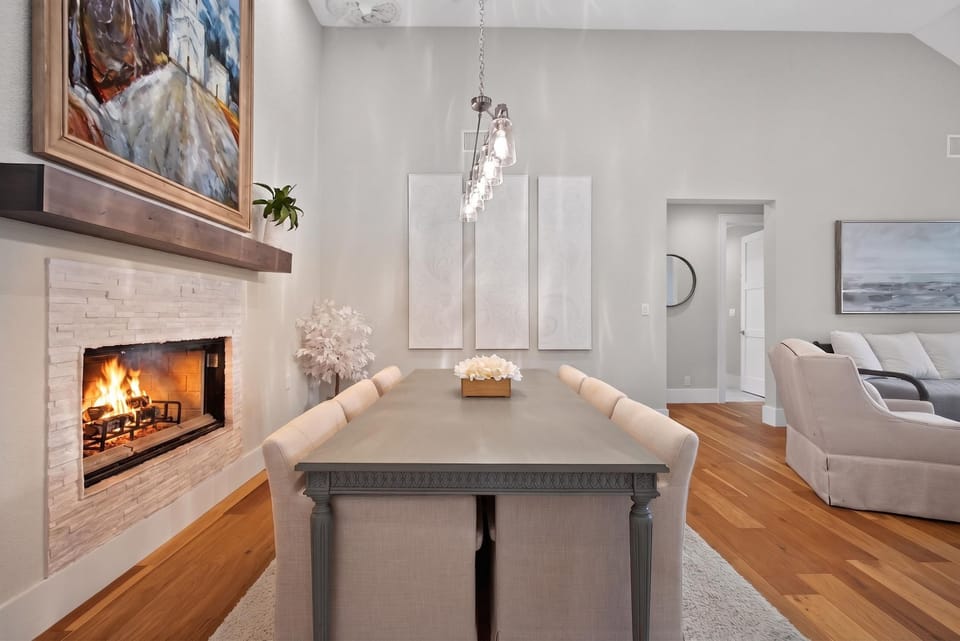 Dining area with table and upholstered chairs beside a lit fireplace.