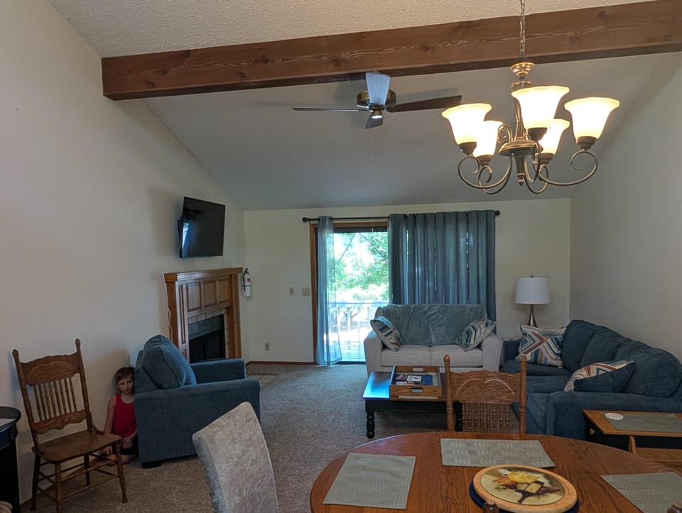 Living area with vaulted ceiling, wooden beam, ceiling fan, and sliding glass doors behind blue curtains.