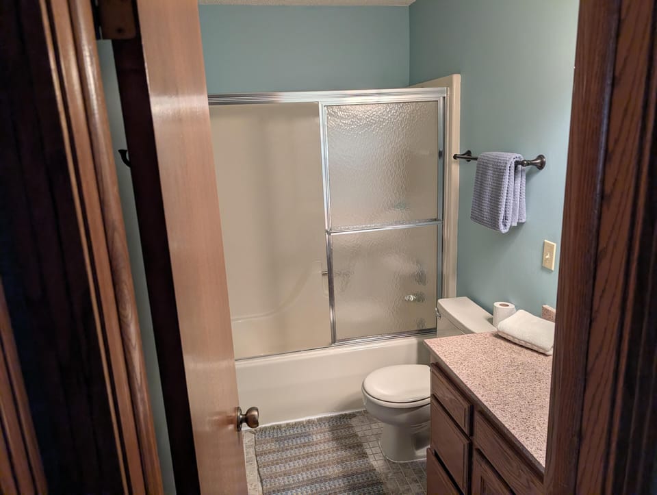 Bathroom with beige tub and sliding textured glass doors, oak cabinetry, granite countertop, and blue walls.