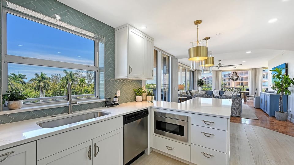 White quartz countertops surround a stainless steel sink and appliances beneath green subway tile backsplash.