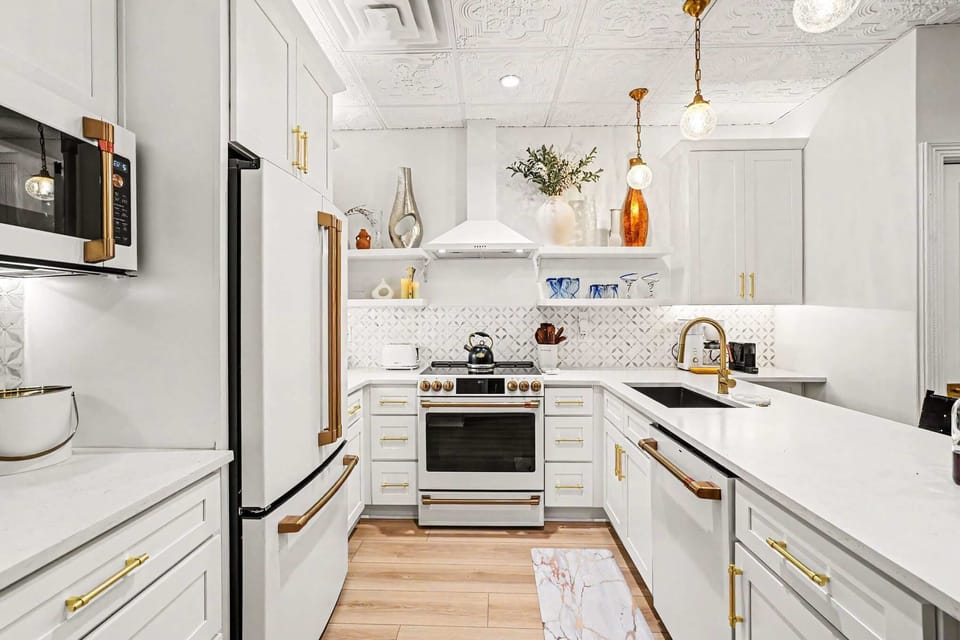 This white kitchen shines with brass and gold accents, high-end appliances, and an oversized island perfect for entertaining, all under a stunning pressed-tin ceiling for character.