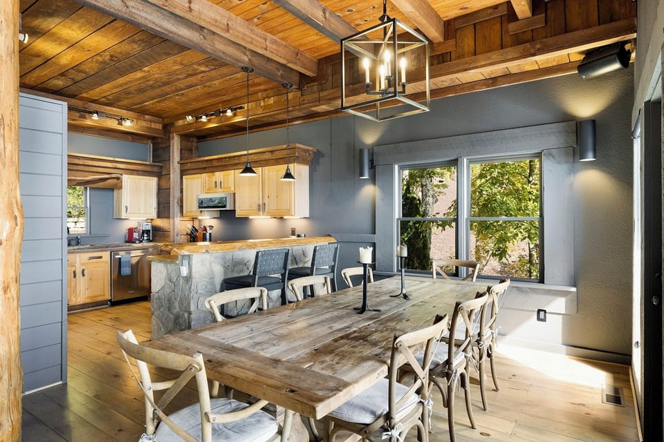 Cook and gather in the same breath. The open kitchen spills into a long farmhouse table under a lantern chandelier — the natural center of the whole house.