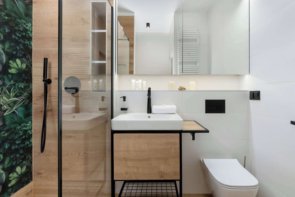A compact bathroom utilizes a floating wooden vanity with a white vessel sink and sleek black fixtures. A glass shower enclosure sits tightly next to the toilet, maximizing the narrow floor plan.