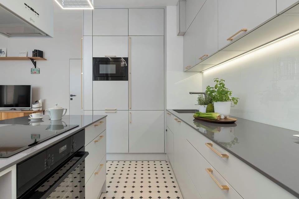 A sleek galley kitchen displays seamless, floor-to-ceiling white cabinetry and a built-in microwave. A clean dark countertop holds a small potted plant, adding a touch of freshness to the minimalist design.
