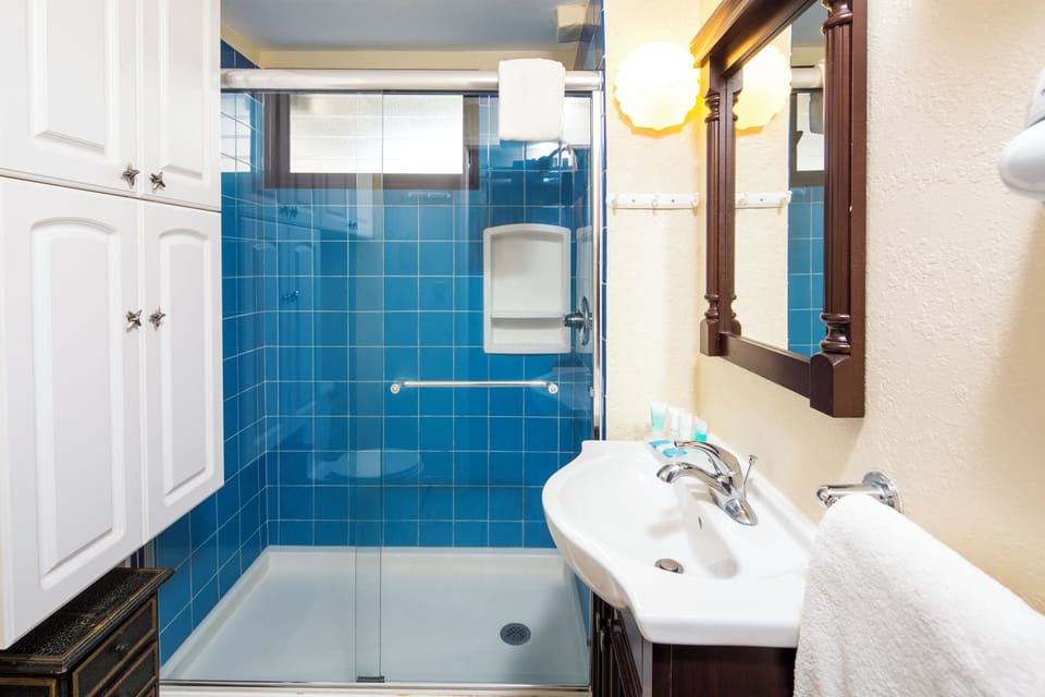 Refresh in your private bathroom with its sleek glass-enclosed shower and vibrant blue tiles. Fluffy towels await, and warm lighting creates a welcoming retreat after a day of exploring.