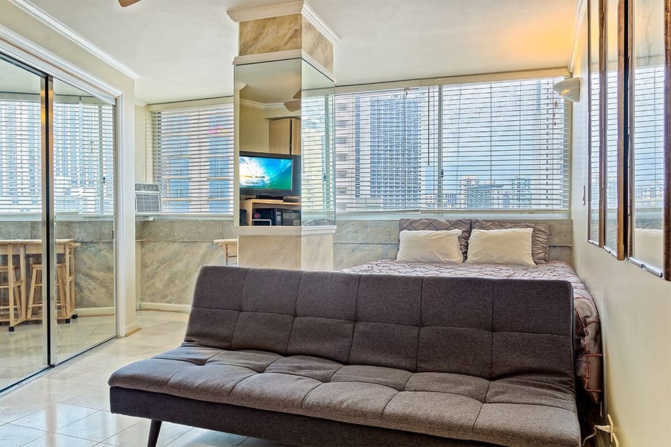 Your bright, modern studio features floor-to-ceiling windows with city views, a plush sofa, comfortable sleeping area, and seamless balcony access—perfect for urban relaxation.