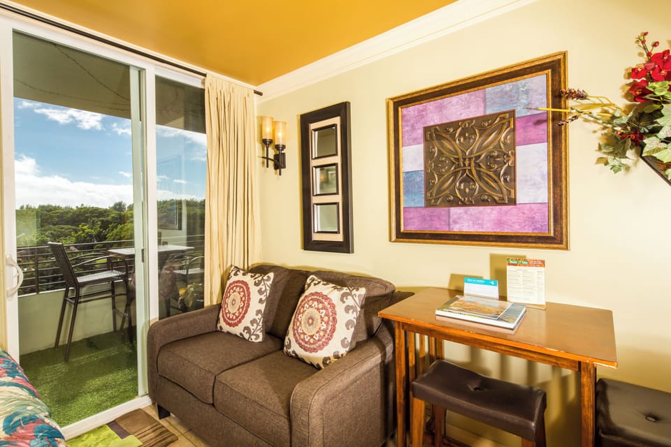 Settle into your cozy living space where sunny skies and lush greenery await just beyond the balcony doors. Plush seating, warm pops of color, and natural light create the perfect spot to unwind.