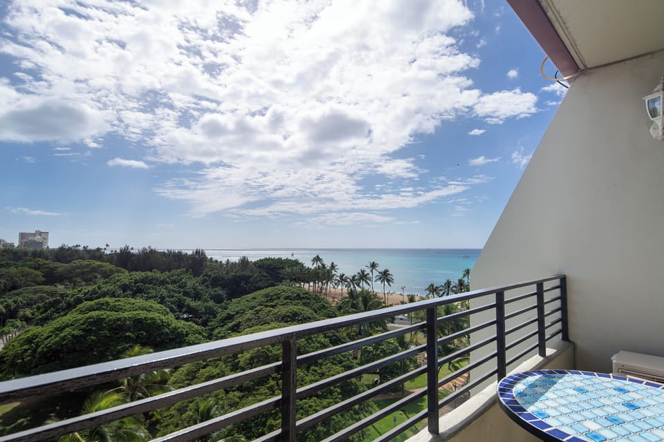 Elevated balcony showcasing sweeping ocean views, lush greenery, and a nearby beach framed by swaying palms.