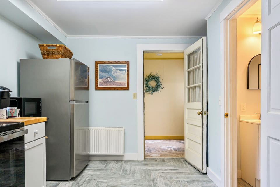 Step inside from the side door straight into the core layout. This view shows how the mudroom connects directly to the kitchen, complete with a full-size stainless steel refrigerator and an easily accessible first-floor half bath for your group.