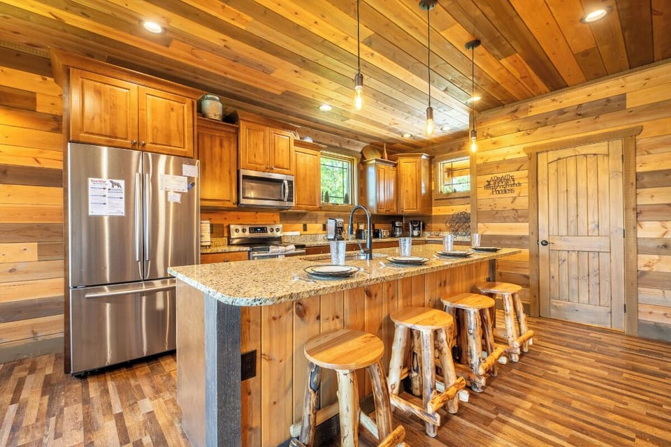 Warm wood surrounds you in this inviting kitchen, where rustic charm meets modern convenience. Gather around the granite island with handcrafted log stools—perfect for morning coffee or preparing meals together.
