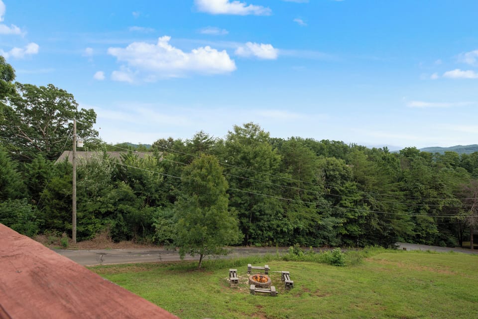 A spacious backyard with a fire pit and seating awaits your outdoor gatherings, framed by lush forest and distant mountain views under expansive skies.
