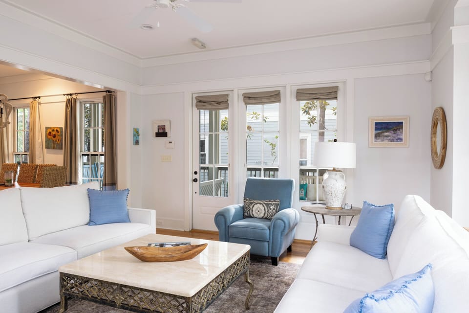 Relax into crisp white sofas and coastal-inspired accents, where soft blue pillows invite you to unwind and French doors frame lush views just beyond your peaceful retreat.