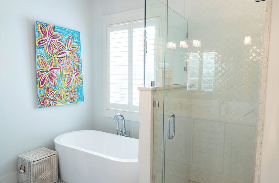 Unwind in your private sanctuary, where a sculptural soaking tub and spacious walk-in shower invite total relaxation. Vibrant artwork adds a cheerful, coastal touch to this serene escape.