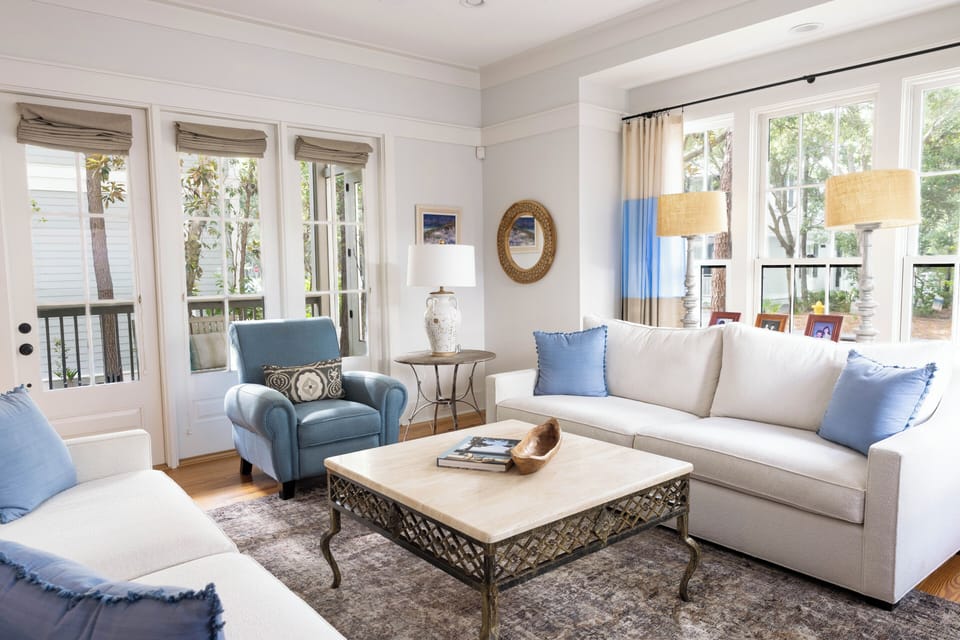 Settle into this inviting living room where coastal blues meet soft neutrals. Large windows flood the space with natural light, revealing treetop views, while plush sofas invite you to unwind after your beach adventures.