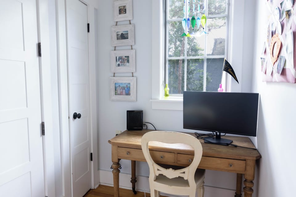 Your cozy workspace awaits with natural light streaming through large windows, a charming wooden desk, and personal photo touches that make this sunny corner feel like home.