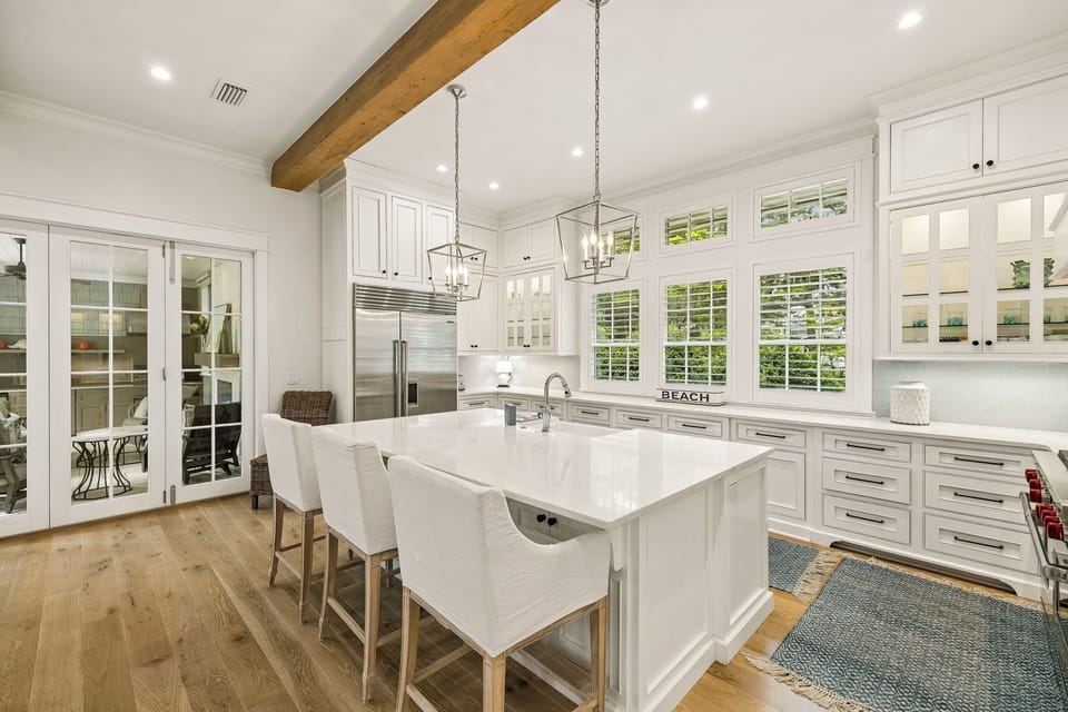 Your gourmet kitchen features pristine white cabinetry, a spacious island with seating, and natural light pouring through plantation shutters—perfect for morning coffee and meal prep.