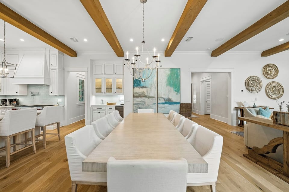 Gather your group around this stunning oversized dining table beneath soaring wooden beams. The open layout flows effortlessly into a bright, inviting kitchen, perfect for preparing meals together.