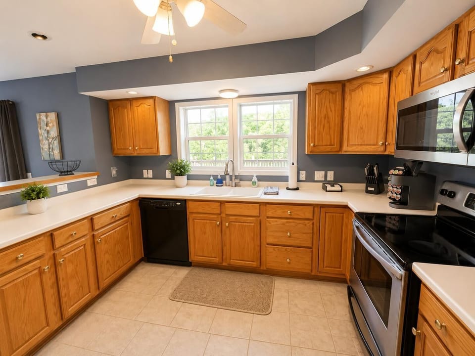 Kitchen with oak cabinets, white countertops, black dishwasher, oven, and a window over the sink.