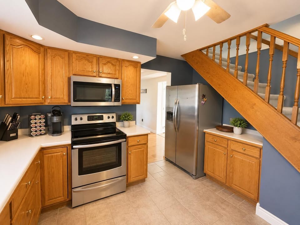 Stainless steel appliances stand against oak cabinetry and slate blue walls beneath a ceiling fan.