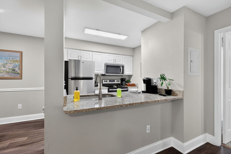 Modern kitchen with stainless steel refrigerator, microwave, Keurig, glass cooktop, coffee station, double sink, and soap dispensers.