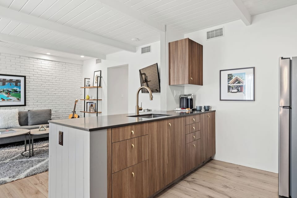 Sleek kitchenette with wood cabinetry, full-size fridge, and open flow to the living area.