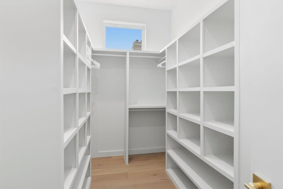 Keep everything in its place in this bright, built-out walk-in closet. Floor-to-ceiling cubbies, hanging space, and warm wood floors make unpacking a breeze, while a sunny window keeps it feeling open and airy.