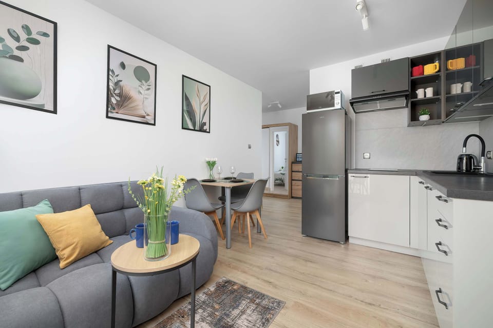 A bright living area a grey sofa and a kitchenette from a wide, angled perspective. Warm wooden flooring flows seamlessly between the living and dining zones.