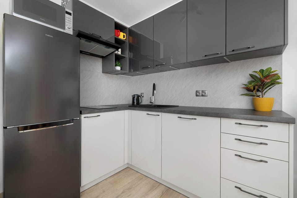 The kitchenette view reveals dark grey upper cabinetry matching the lower units. A wooden countertop extends into the corner space efficiently.